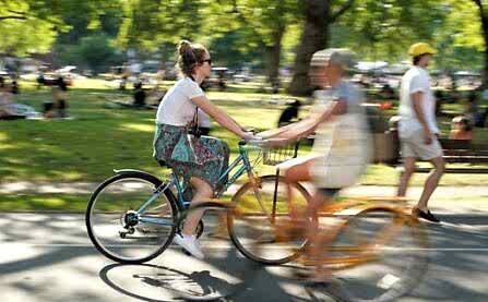 Woman on yellow bike cycling through park in sunshine